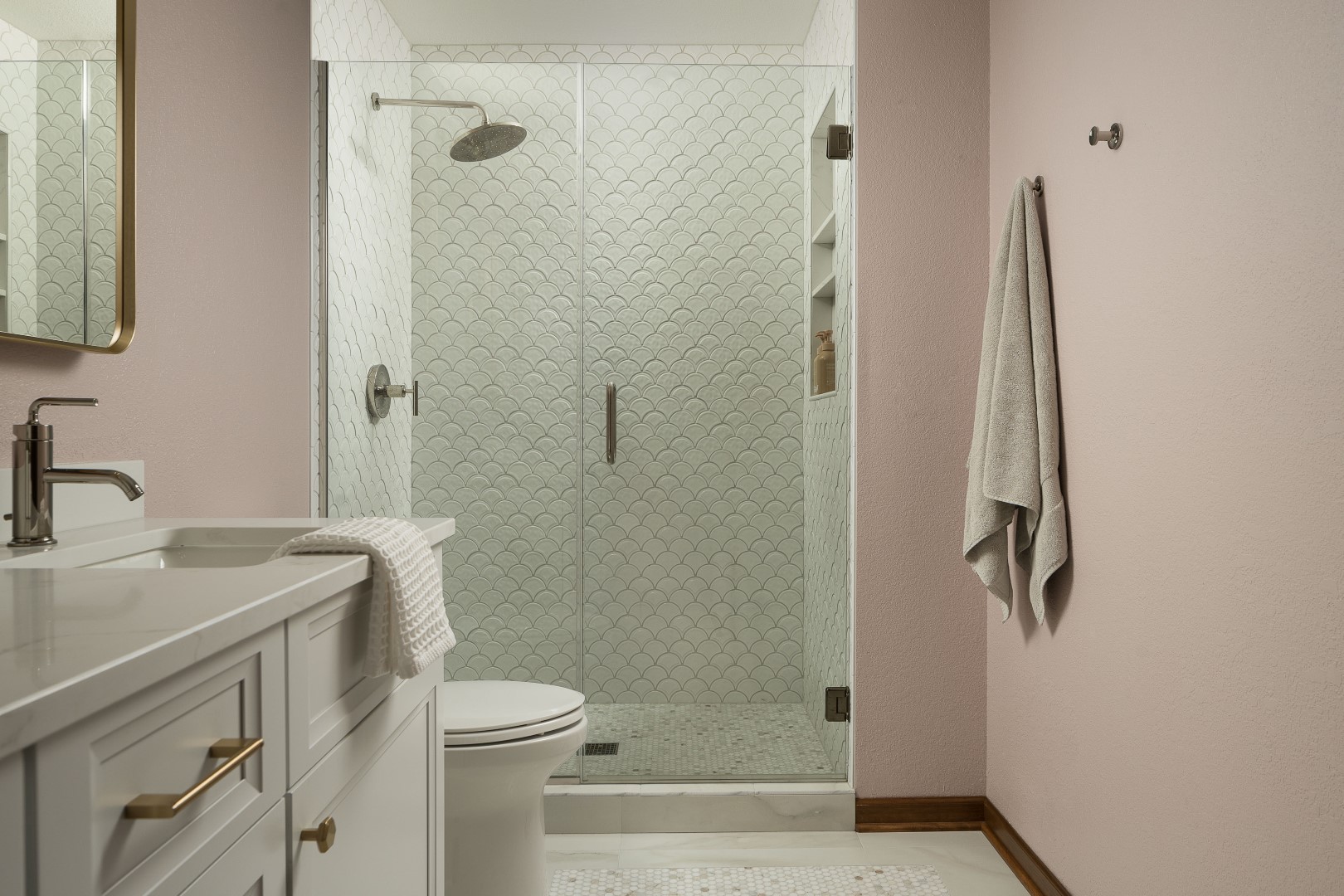 A modern bathroom with white vanity, glass shower, patterned tiles, and beige walls. A towel hangs on the wall, creating a cozy atmosphere.