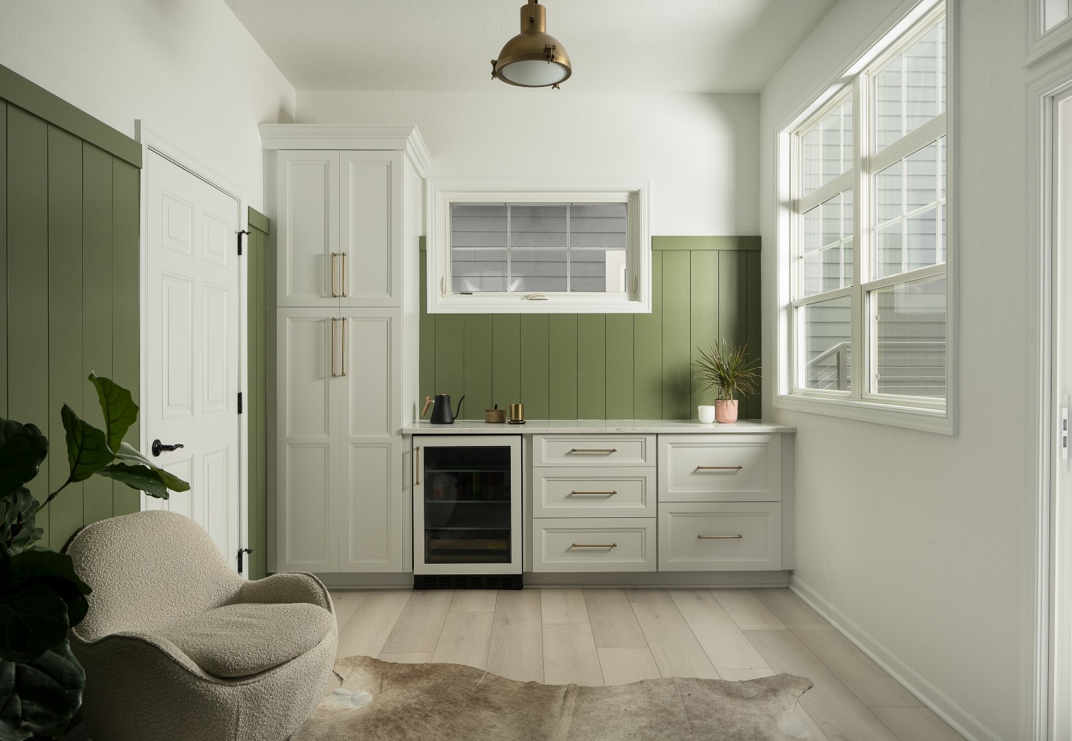 Cozy room with green paneling, large white cabinets, and a cream chair. Light wooden floor and window provide natural ambiance.