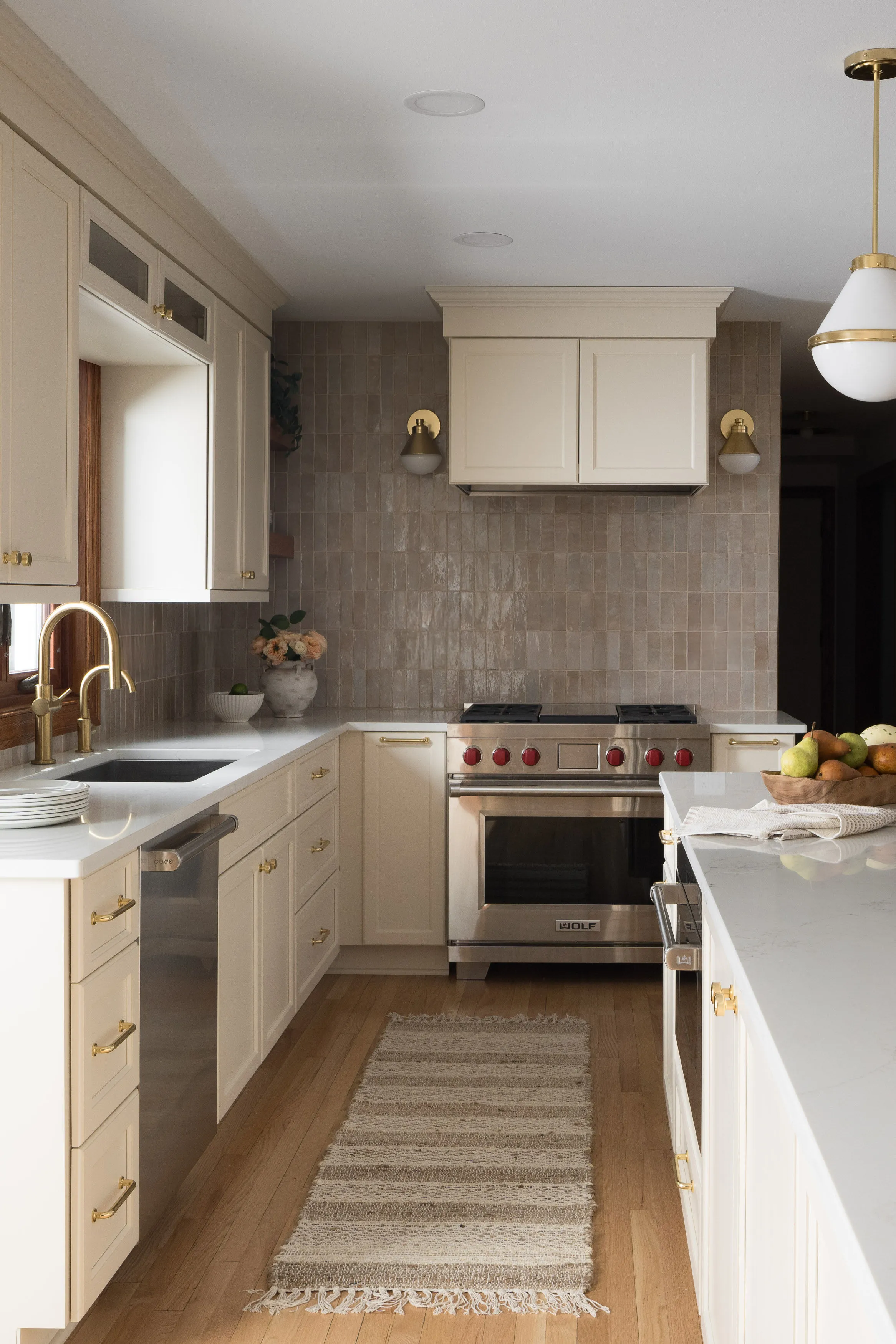 Elegant kitchen with cream cabinets, stainless steel appliances, and a striped rug. Brass fixtures complement the wood flooring and soft lighting.