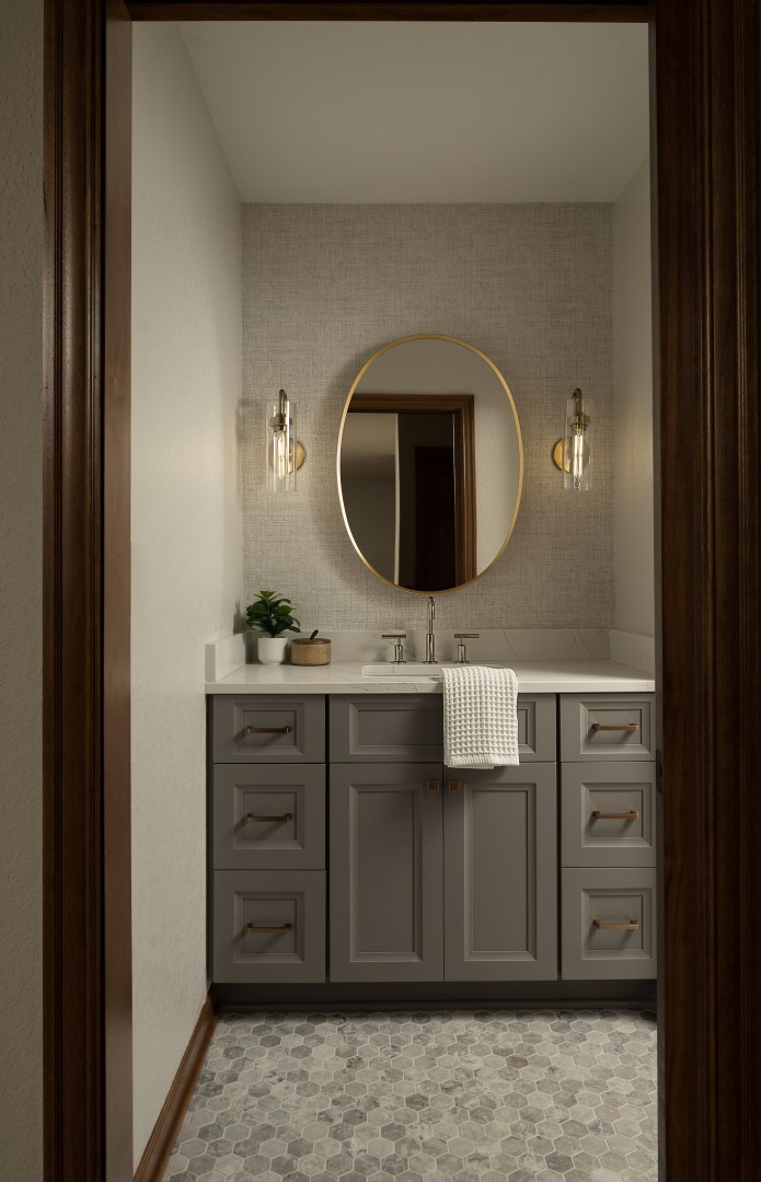 A modern bathroom with a gray vanity, round mirror, and elegant lighting. Tiled floor and wall accents create a sophisticated ambiance.