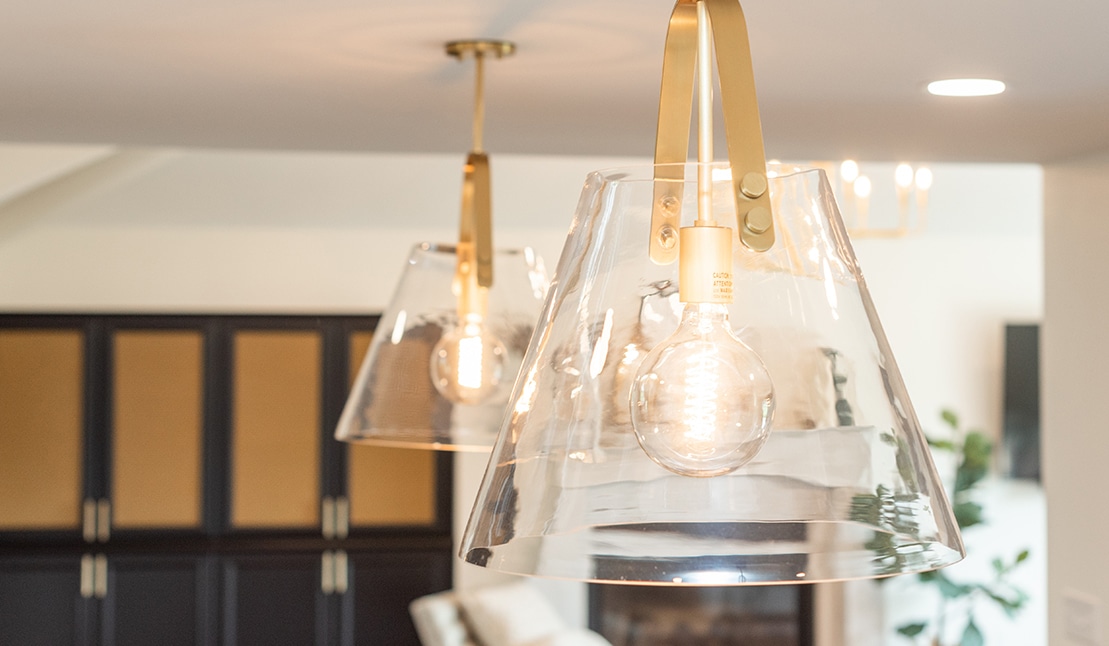Modern living room interior with two transparent pendant lights, focused on warm bulbs. Background includes cabinets and blurred decor elements.