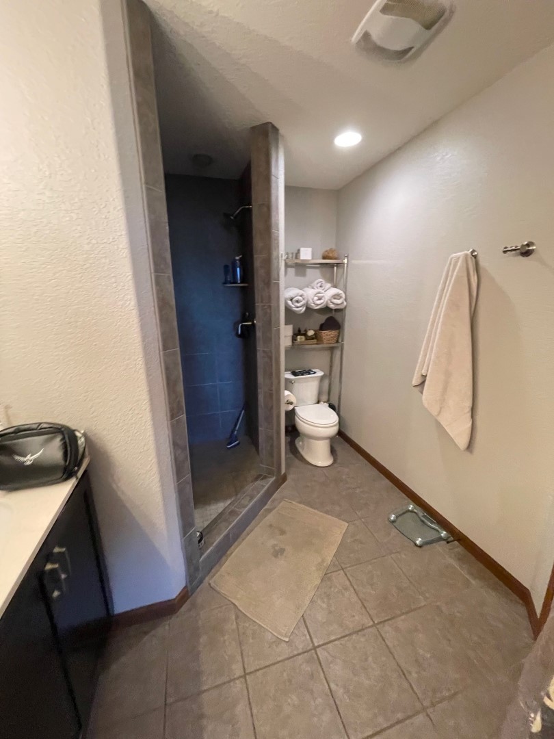 A modern bathroom with a glass shower, tiled floor, sink, toilet, and towel rack. Neutral tones create a calm, clean atmosphere.