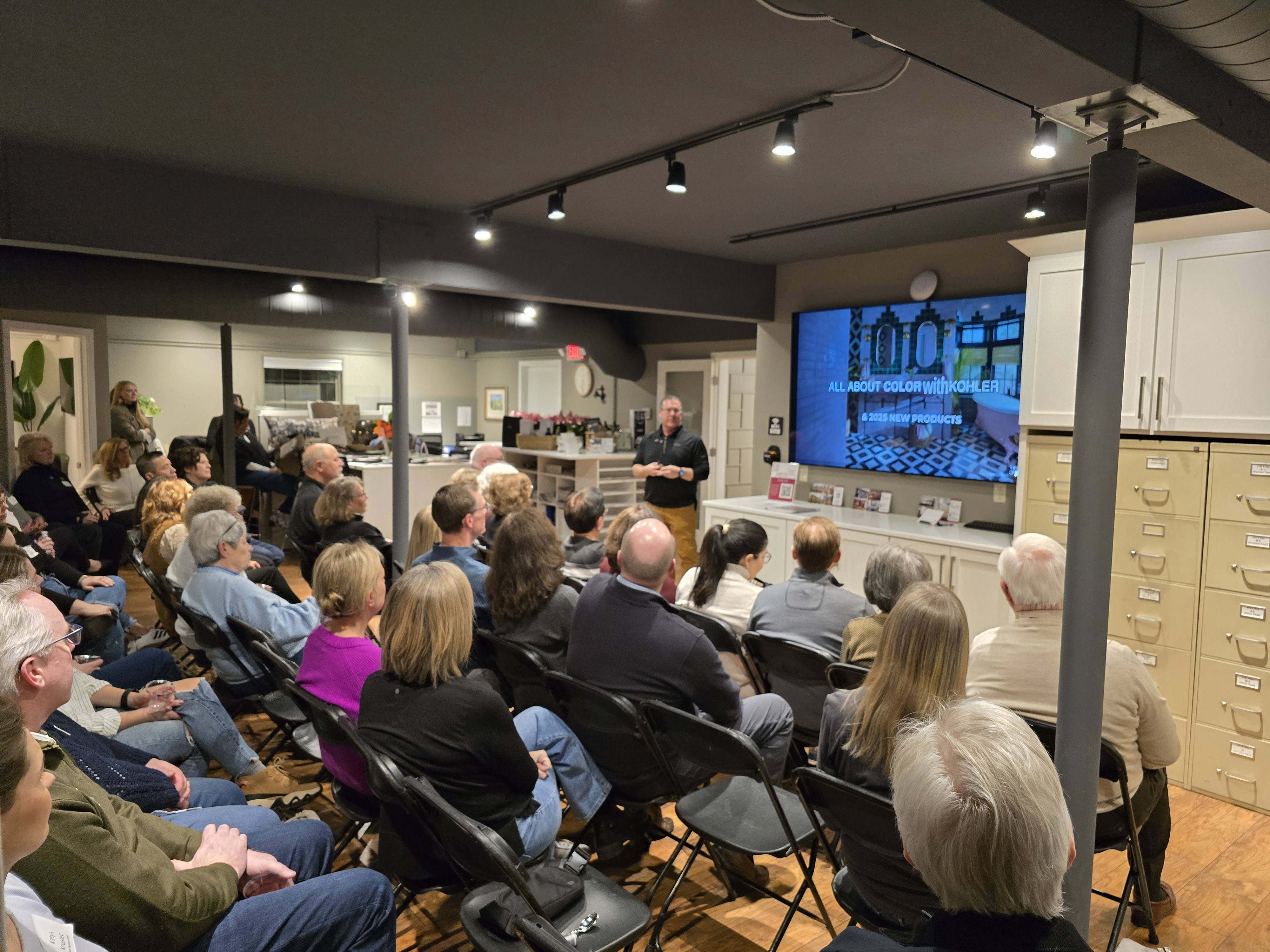 A person presents to a seated audience in a meeting room, with a screen displaying "All About Color with Kohler" and "2023 New Products."