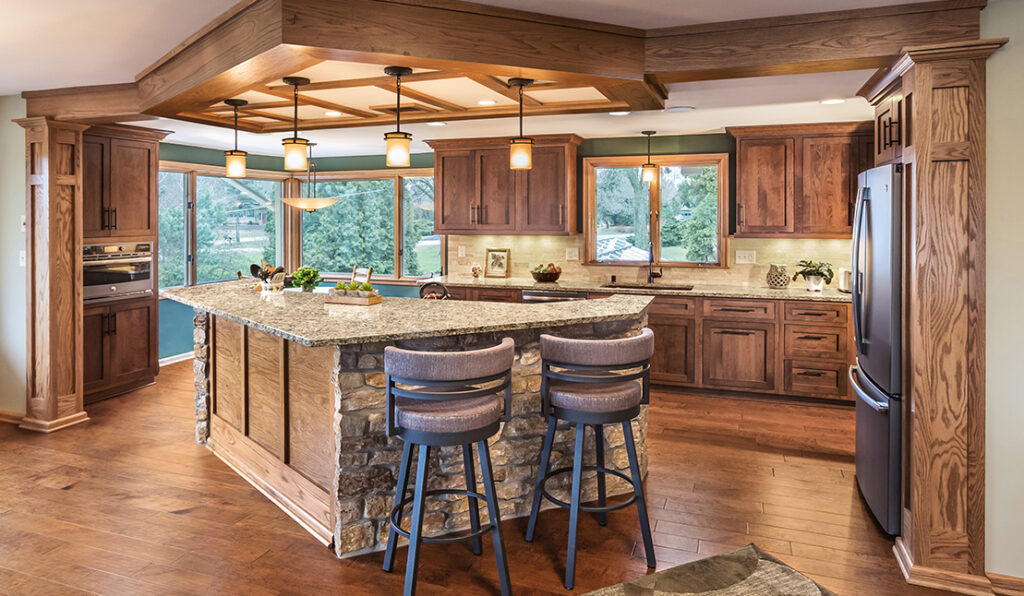 Midcentury modern kitchen remodel with wood floors, woodgrain cabinets, and large special-shaped island with stone underneath and granite countertop. Large casement windows in the far corner.