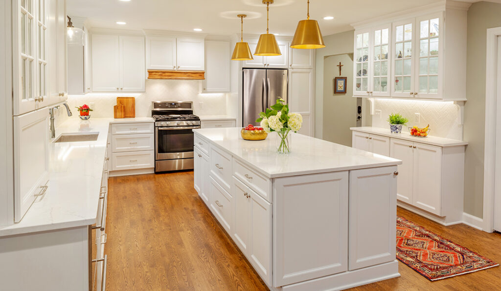 Renovated kitchen featuring new wood flooring, white cabinetry, white stone countertops, and modern gold fixtures.