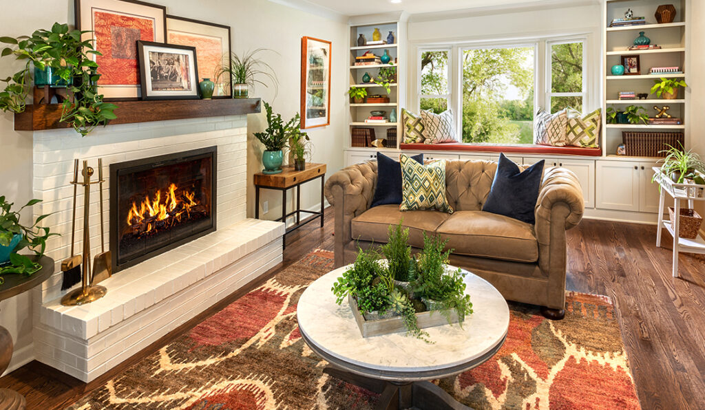 Recently remodeled living room with new flooring, a lit fireplace in a white brick mantel, built-in shelving, and decorative plants throughout.