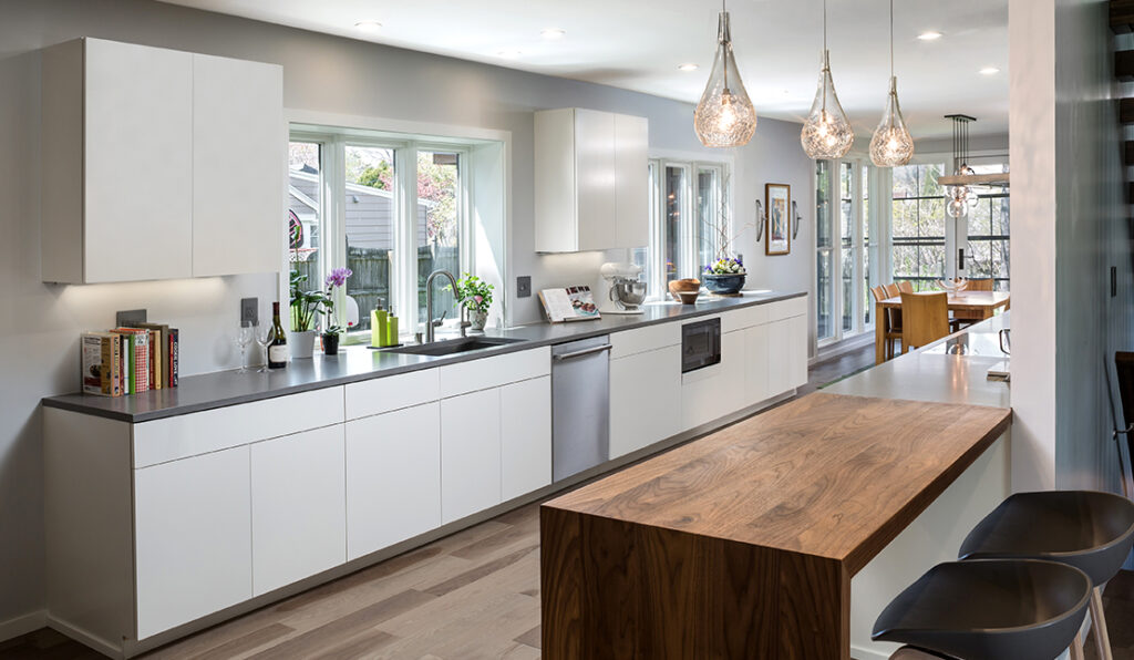 Remodeled home kitchen featuring new wood flooring, white modern cabinetry, gray and butcher-block countertops, and pendant lighting.