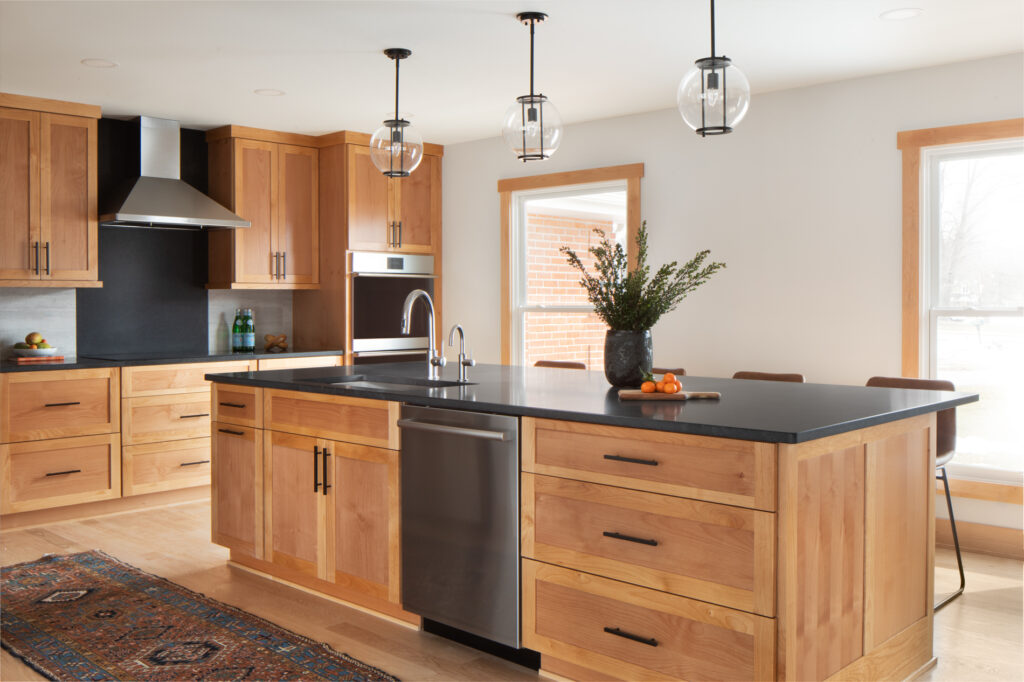 Freshly remodeled kitchen in a home. A new island, fixtures, light wood flooring, light woodgrain cabinetry, black countertop, pendant lights..