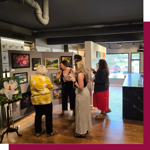 Four people admire colorful artwork in a gallery setting. Paintings are elegantly displayed on walls. Bright lighting highlights the creative atmosphere.