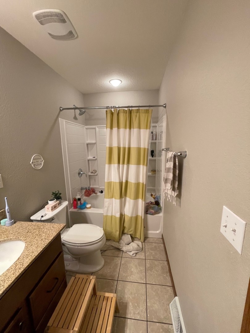 A small bathroom with a shower, striped curtain, tiled floor, wooden step stool, and a countertop with sink. Neat and organized.