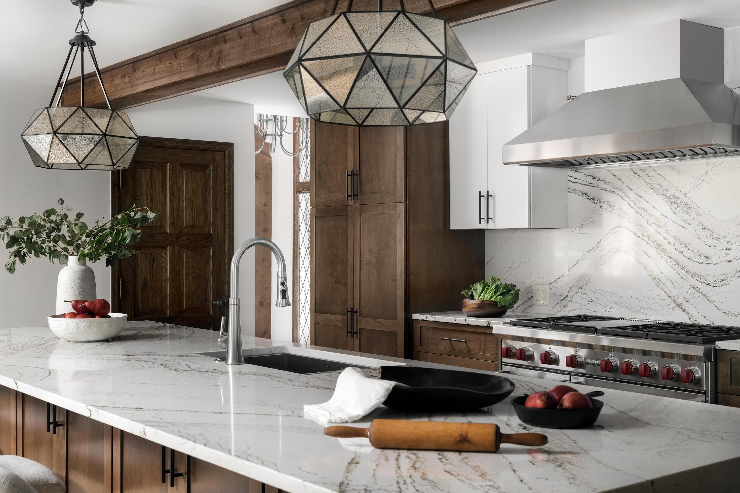 Modern kitchen with marble countertops, wooden cabinets, geometric pendant lights, stainless steel appliances, and decorative bowls of fruit. Elegant and minimalist design.