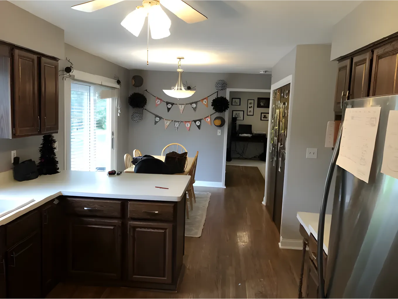 A kitchen with white countertops, wooden cabinets, and dining area. Decorative banners and wall art enhance the modern space. No landmarks present.