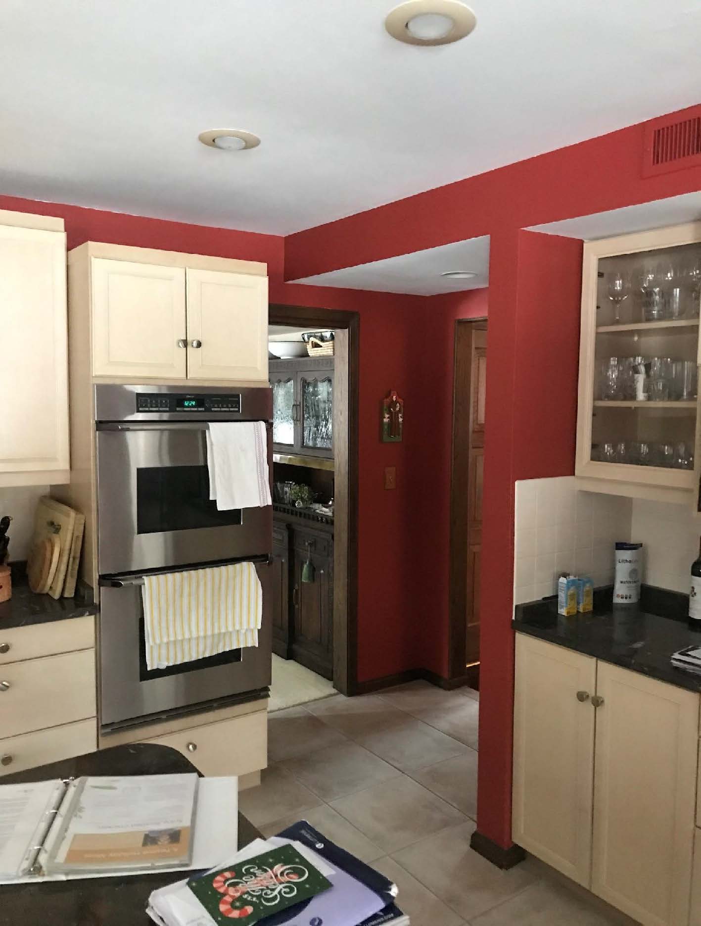 A cozy kitchen with red walls, stainless steel oven, white cabinets, and tile flooring. A hallway leads to another room.