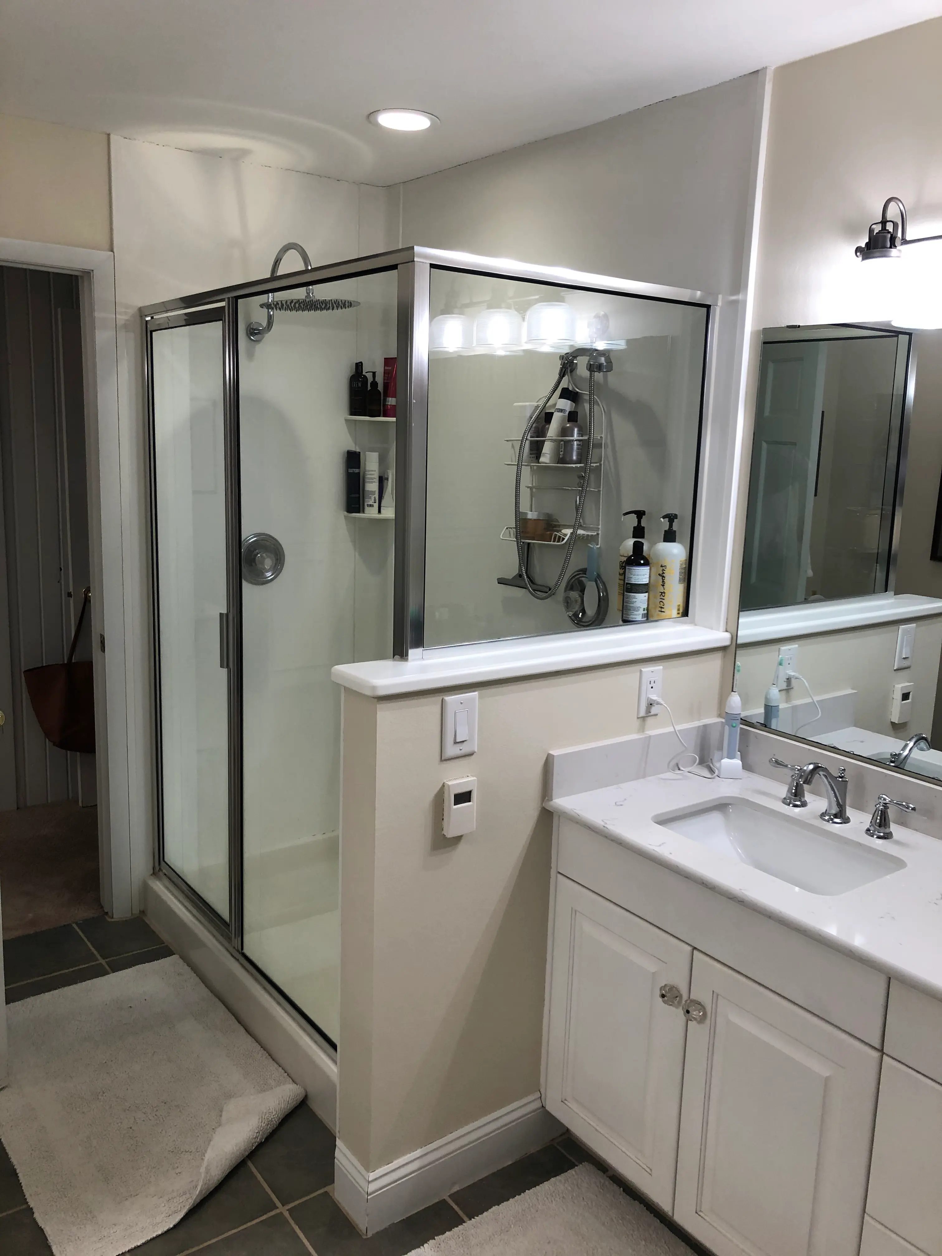 A modern bathroom featuring a glass-enclosed shower, a white vanity sink with a mirror, and various toiletries arranged on shelves and the counter.