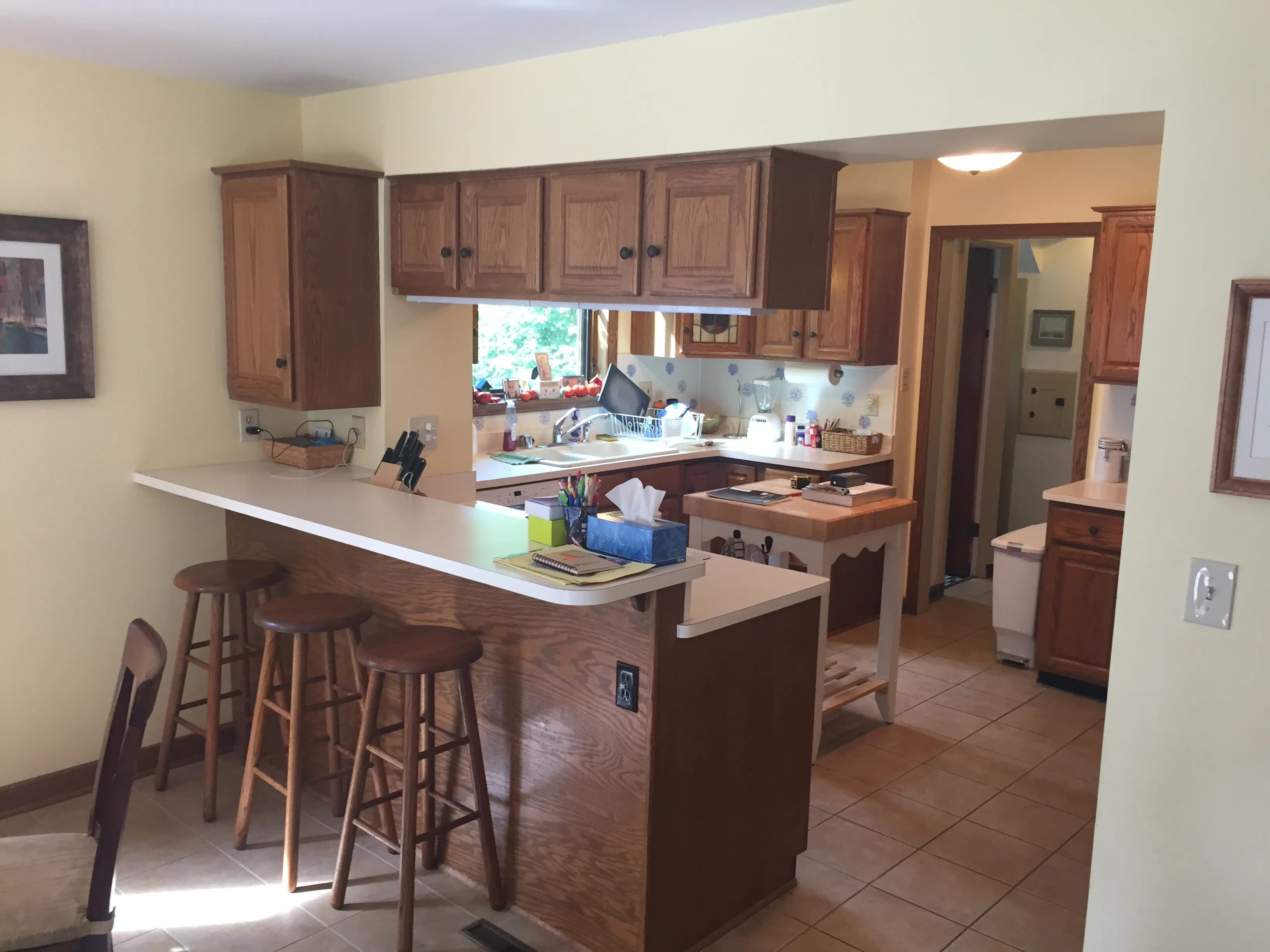A kitchen with wooden cabinets, a breakfast bar, bar stools, and various kitchen items. Light yellow walls create a warm ambiance.