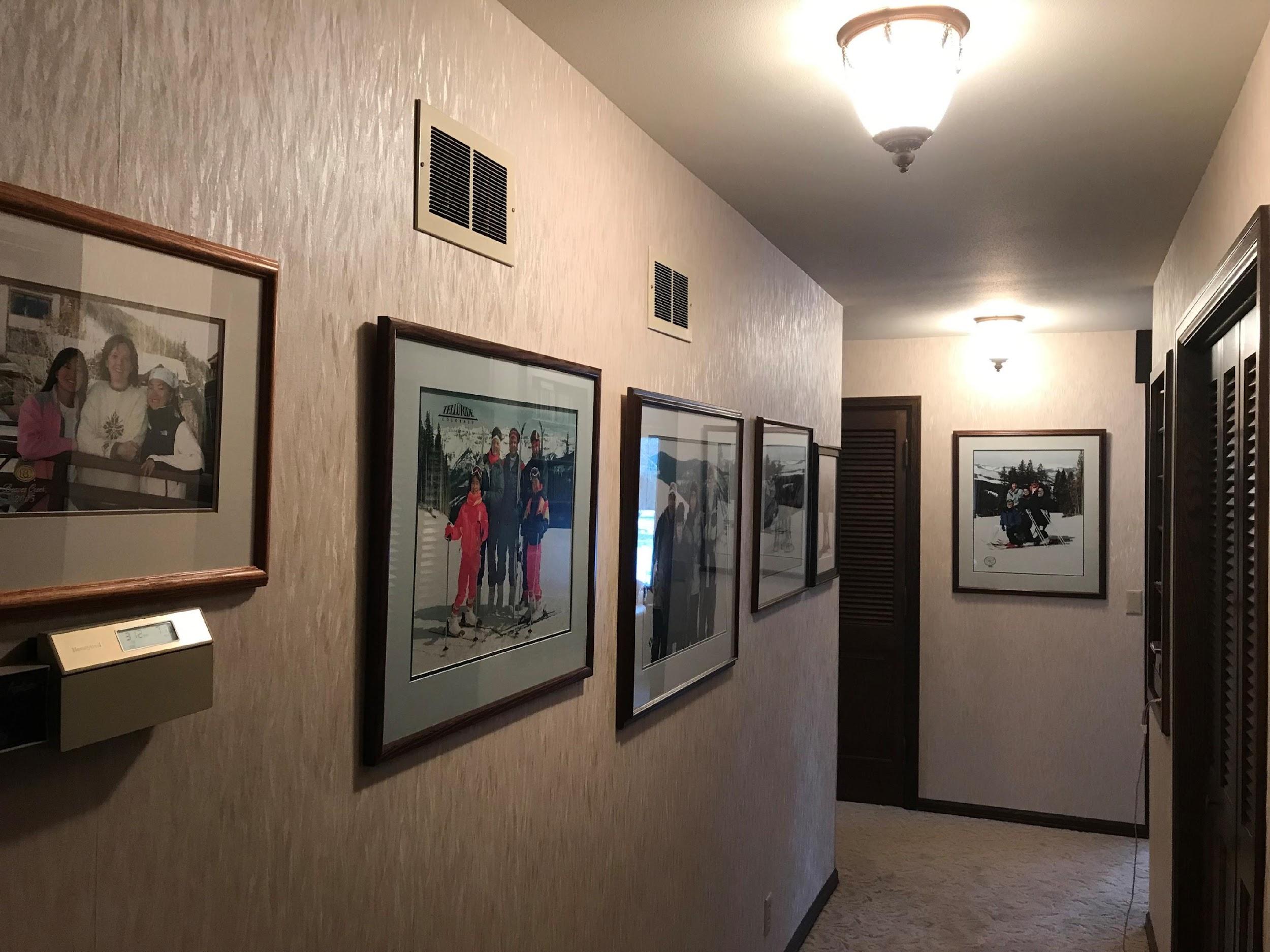 A hallway with framed photographs of people skiing. Warm lighting and closed wooden doors create a cozy, personal atmosphere.