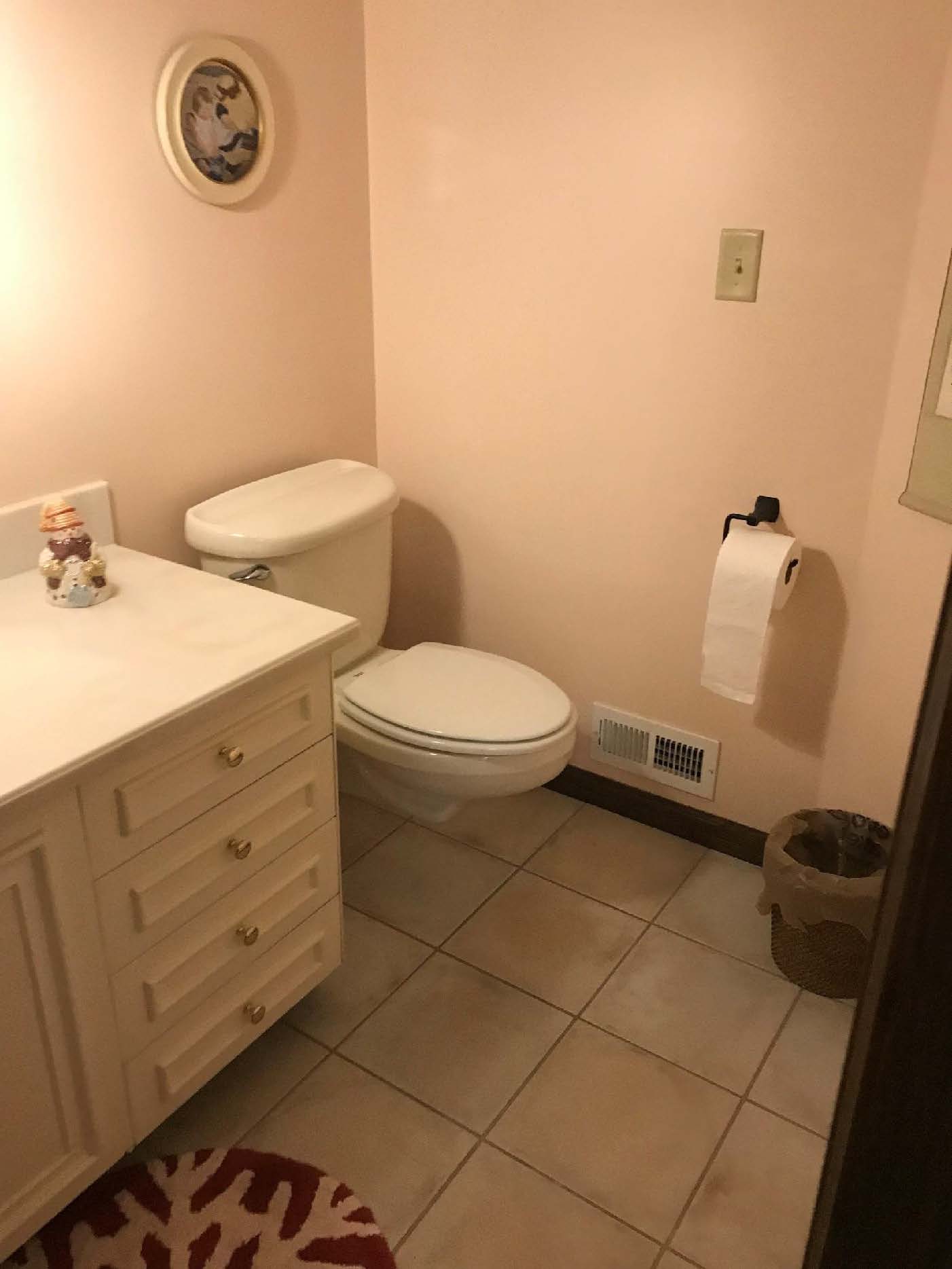 A small bathroom with light pink walls, featuring a white toilet, sink with cabinetry, wall decor, and tiled floor.
