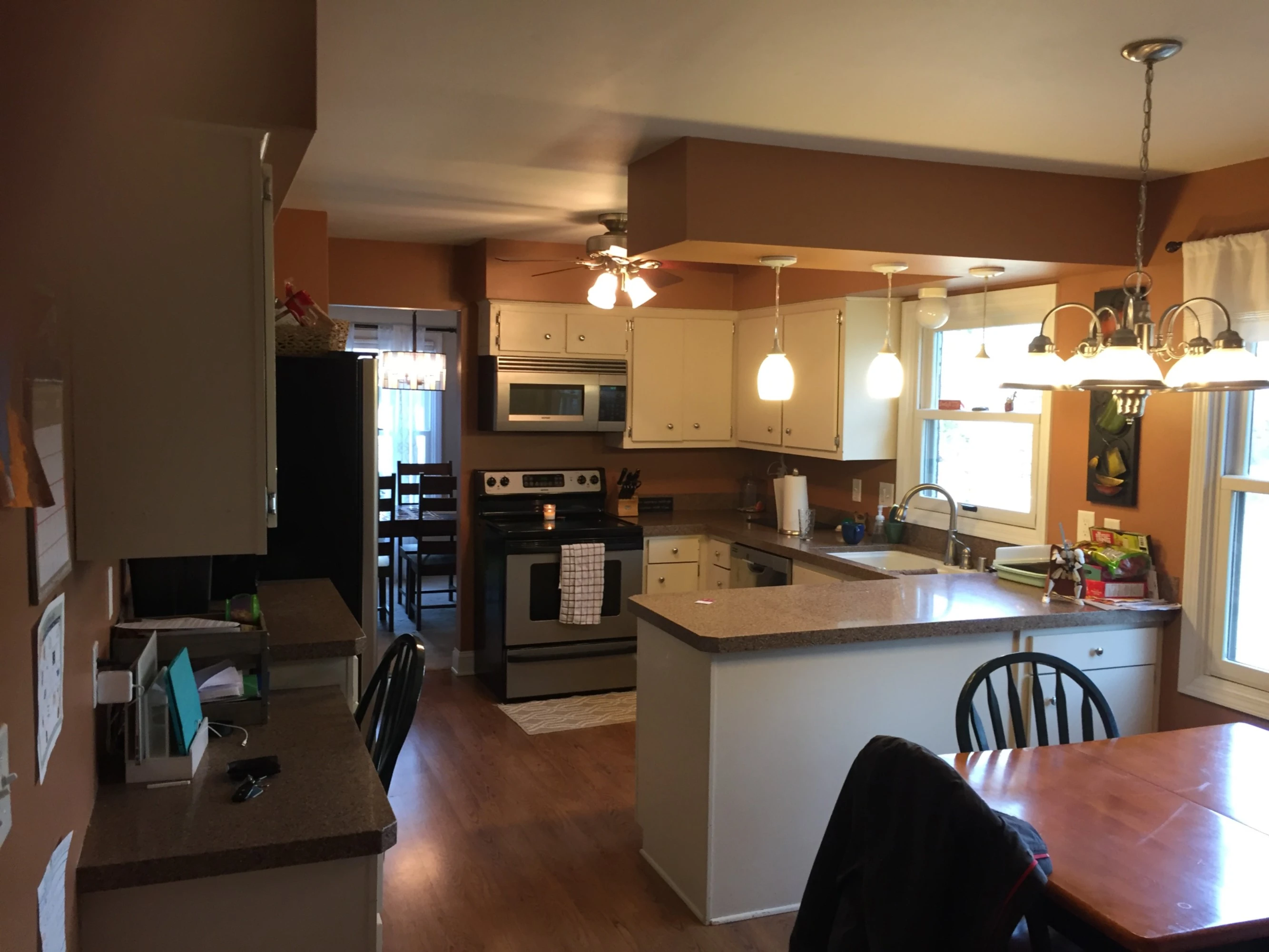 A cozy kitchen with brown walls, white cabinets, and wooden flooring. Includes a dining table, ceiling lights, and modern appliances.
