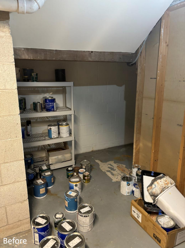 Cluttered room with paint cans on floor and shelf, unfinished walls, exposed ceiling beam, and boxes. Basement storage area with concrete floor.