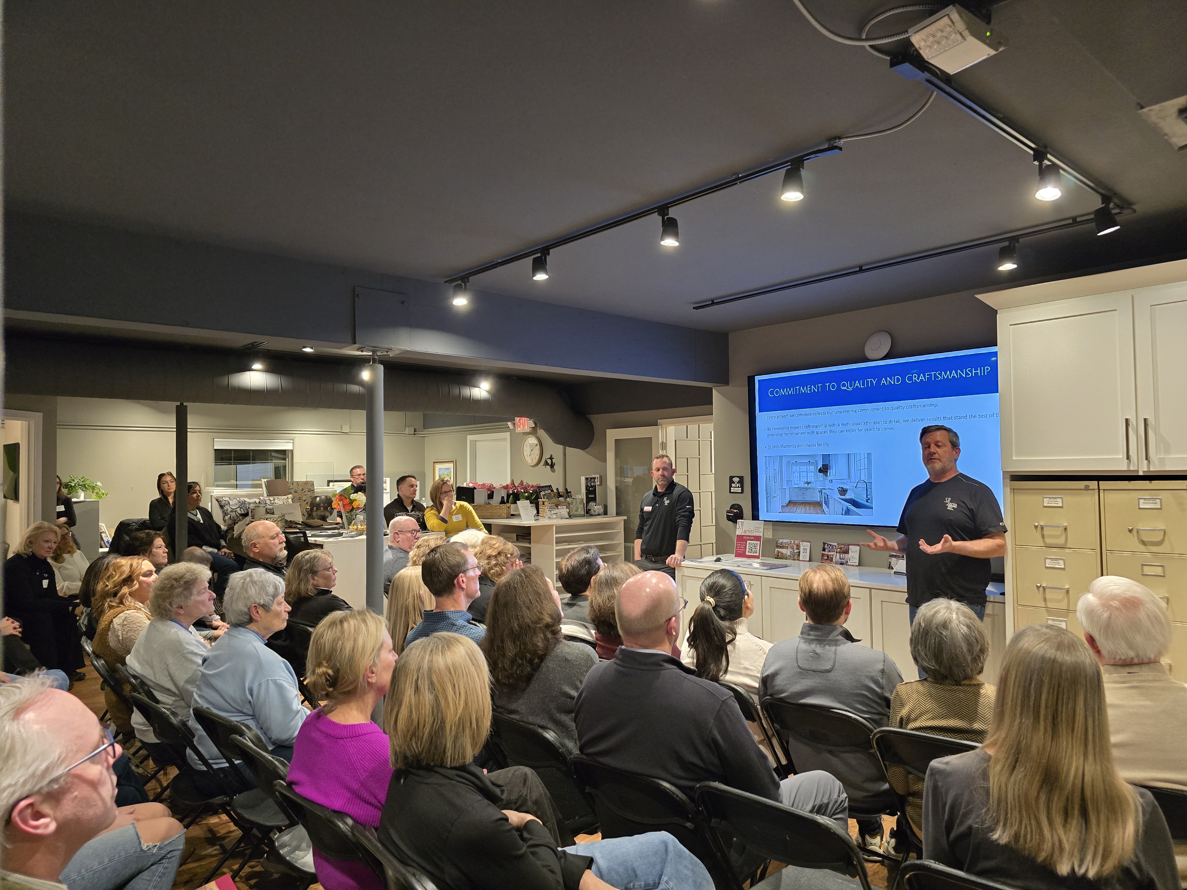 A group of people attending a presentation in a room, with a person speaking in front of a screen about craftsmanship.