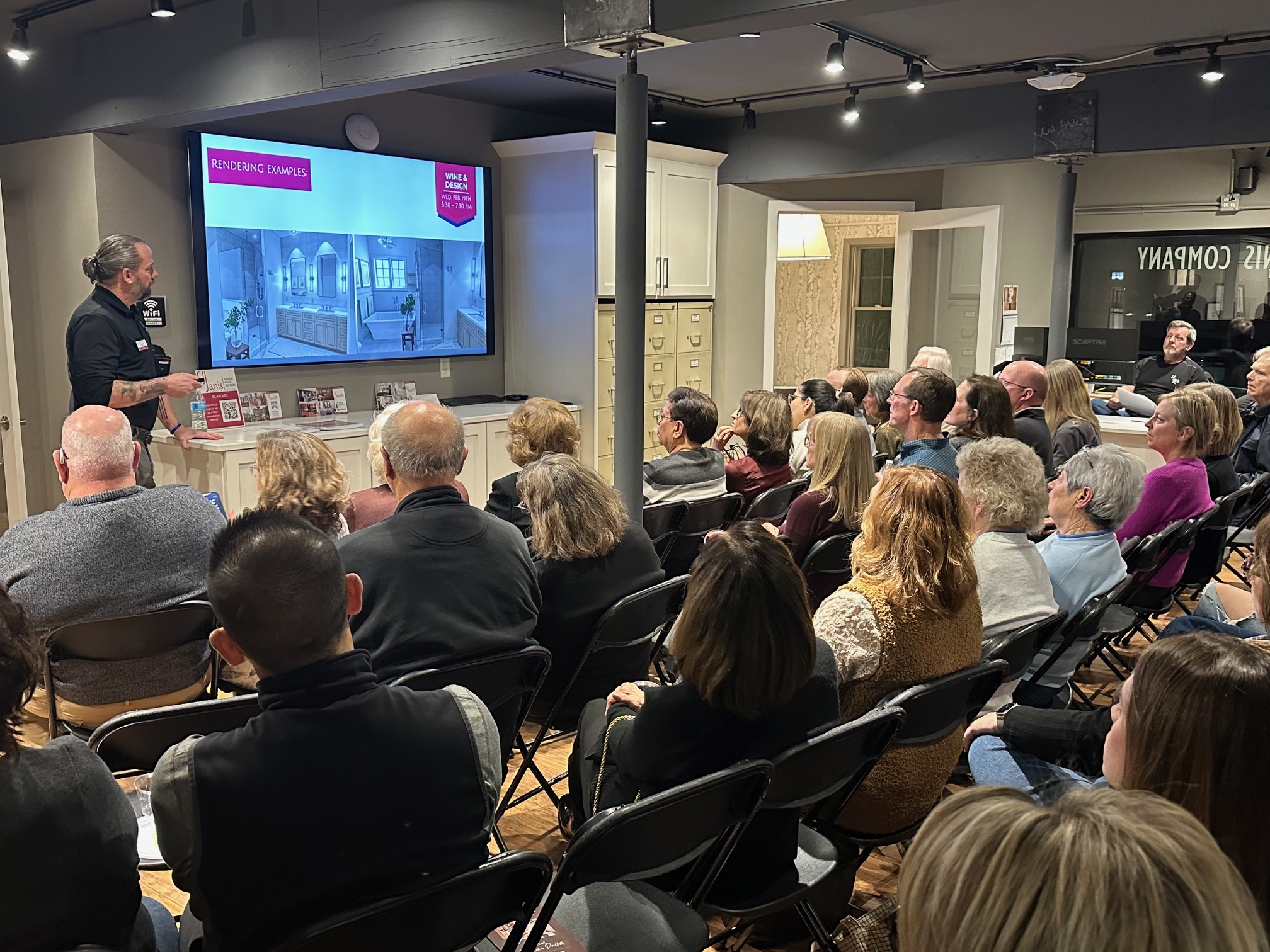 A person presents to an attentive audience in an indoor setting, showcasing rendering examples on a large screen.