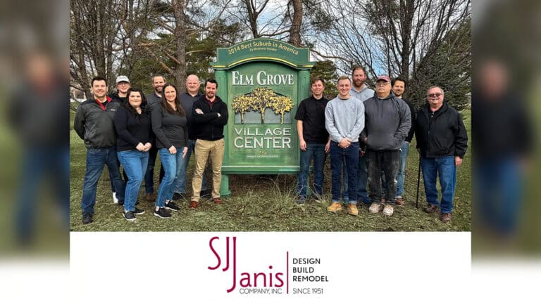 A group of people standing in front of the Elm Grove Village Center sign. Trees are visible in the background.