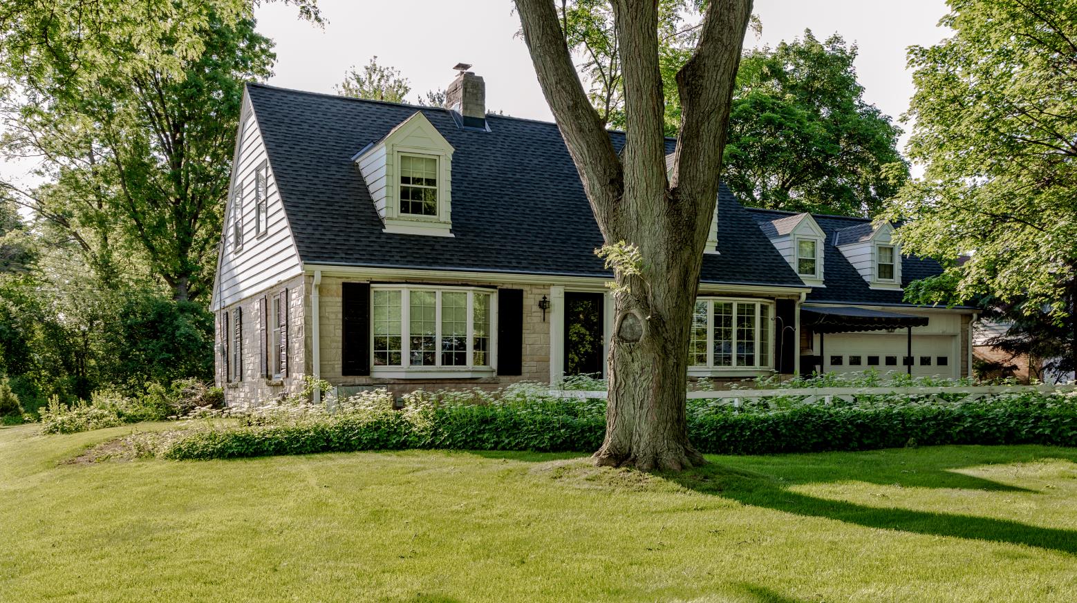 Charming suburban house with gabled roof, surrounded by lush greenery and trees, exuding a peaceful and inviting atmosphere on a sunny day.