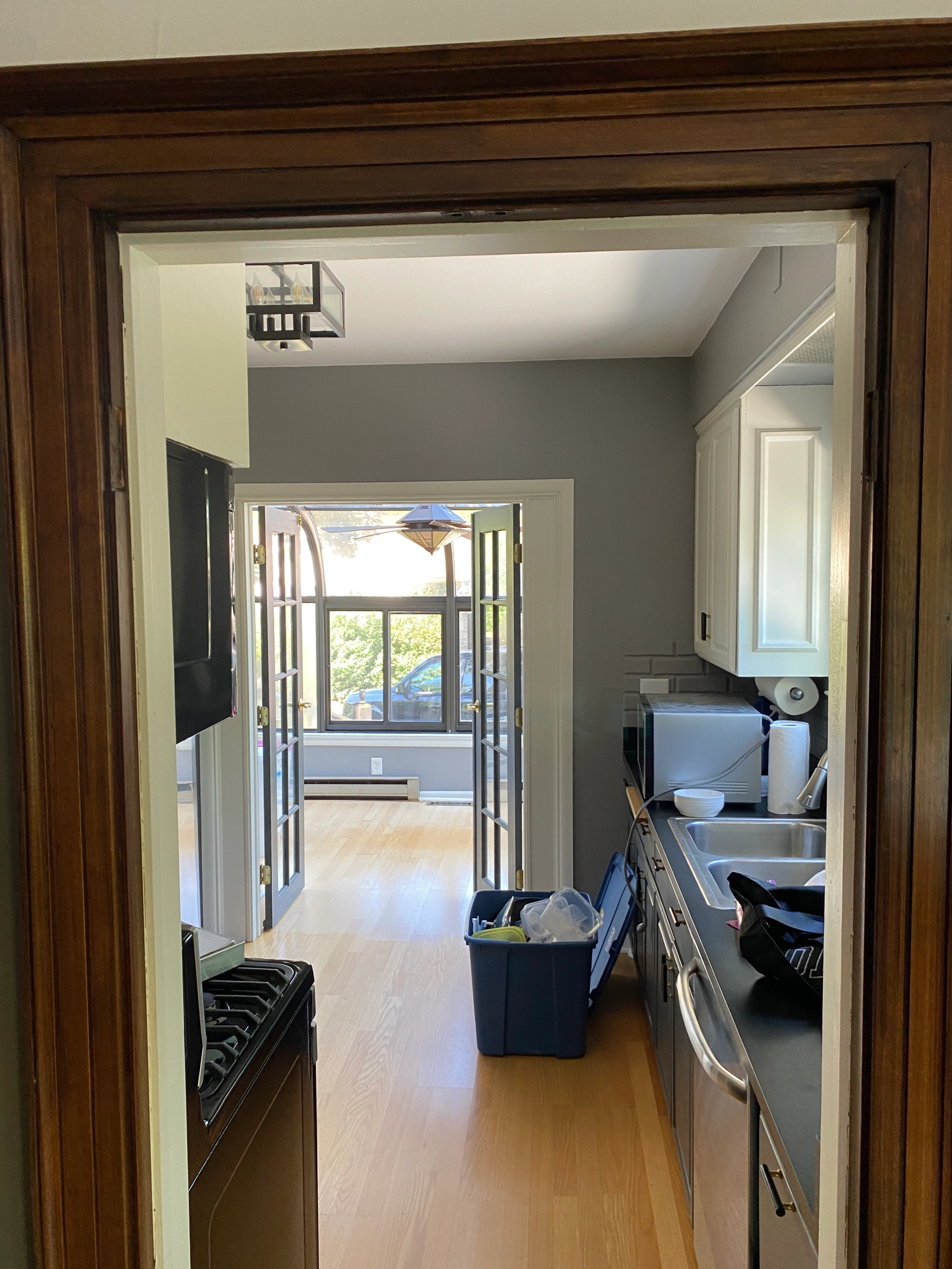 A view through a kitchen entrance shows French doors leading to a bright room with wooden floors and a scenic window view.