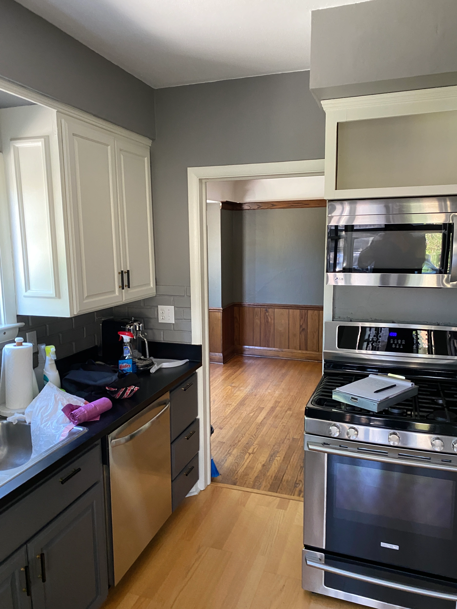 A modern kitchen features stainless steel appliances, white cabinets, and black countertops, with a view into an adjacent room with wood paneling.