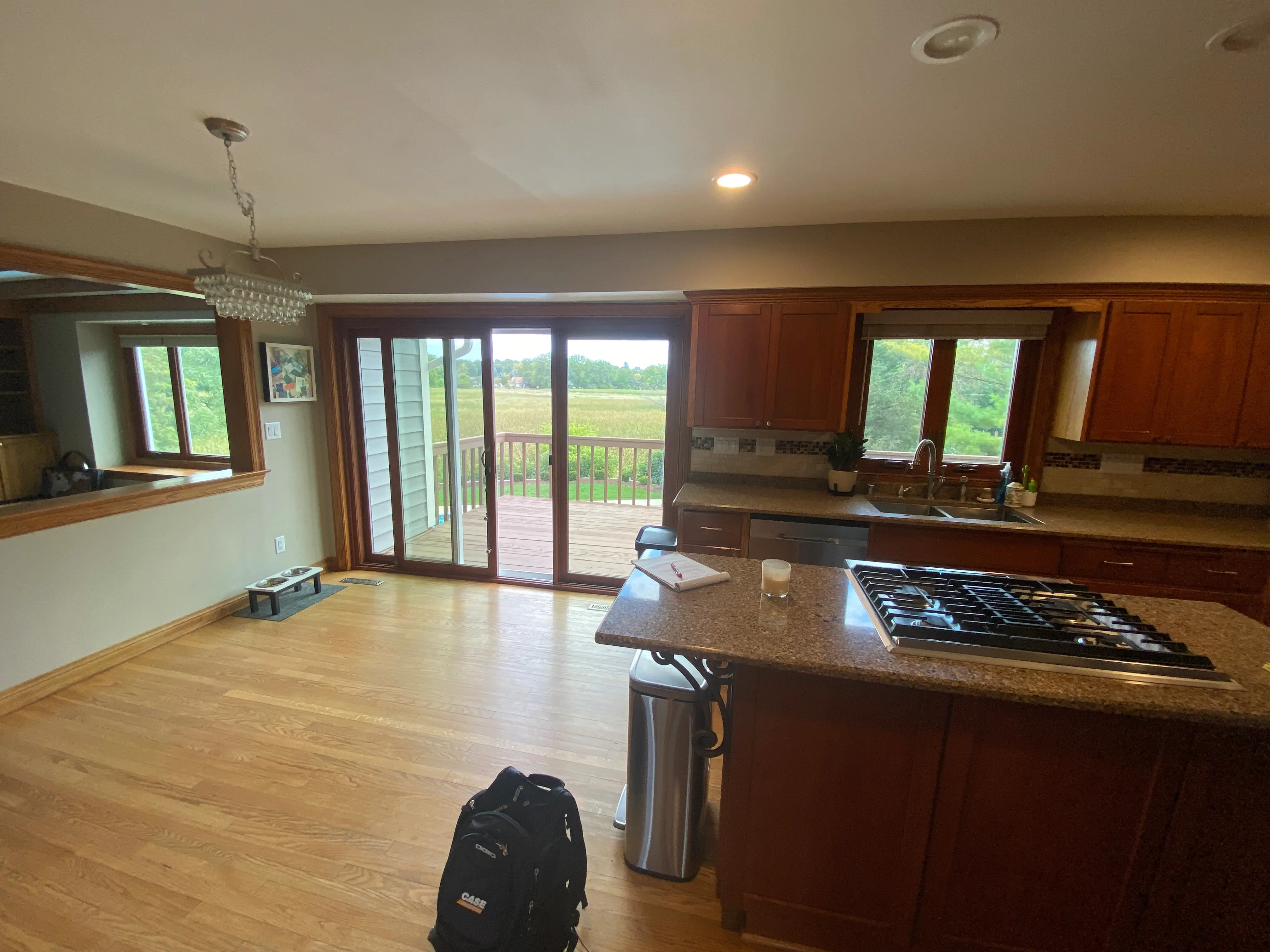 Kitchen with wooden cabinets, island stove, and sliding glass doors leading to a patio with outdoor view. Backpack on wooden floor.