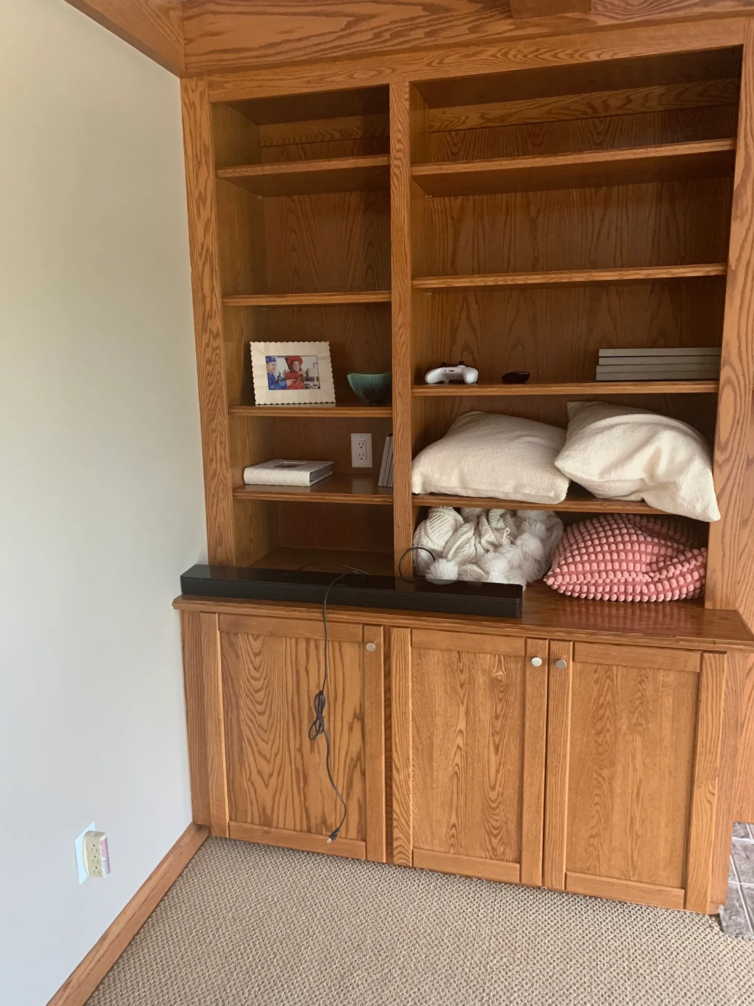 Wooden shelves with decorative items, including a photo of a person, books, and pillows. Carpeted floor visible at the bottom.