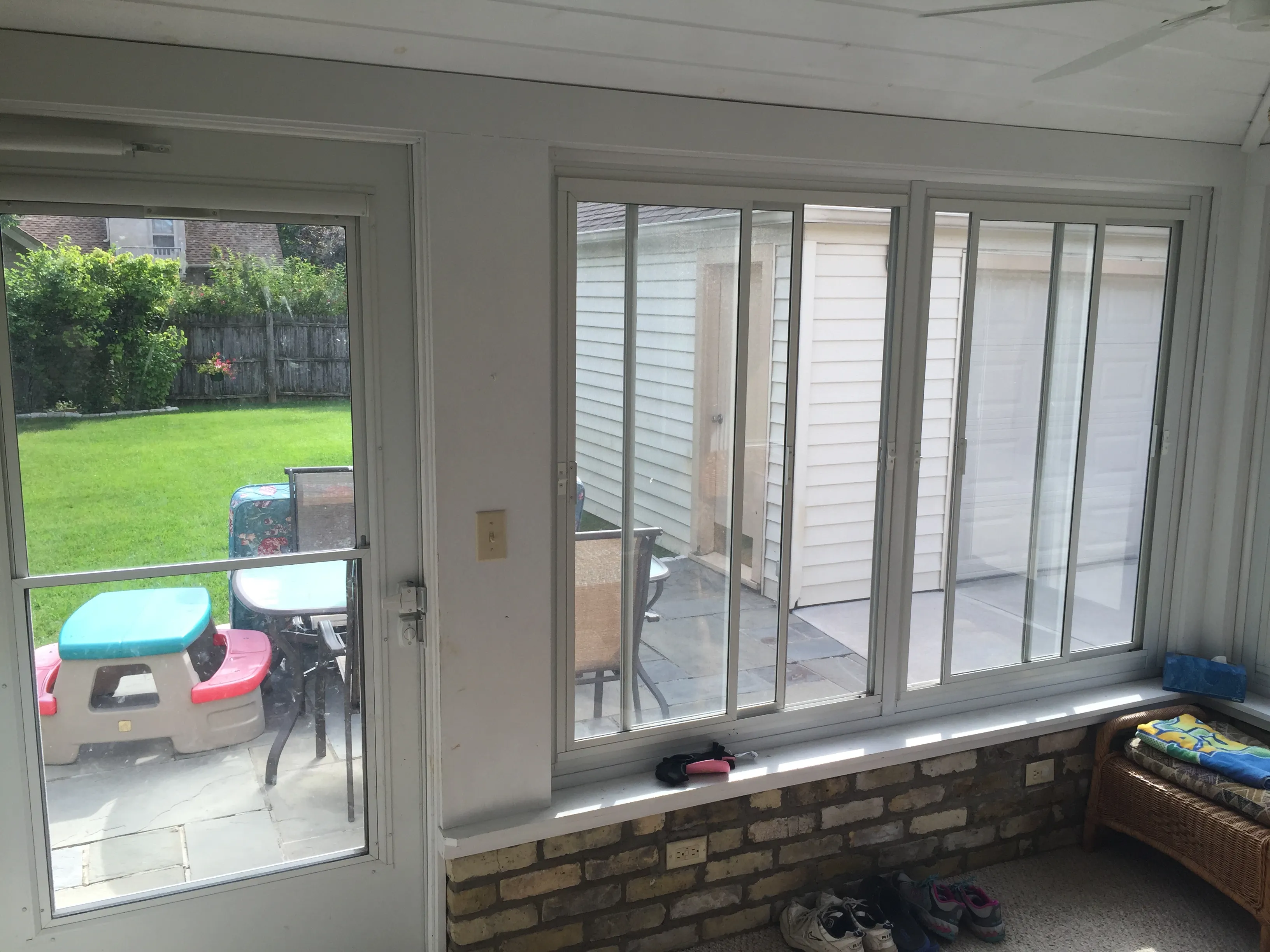 A sunroom with sliding glass doors opens to a backyard featuring children's play furniture and a detached garage. Shoes are on the floor.
