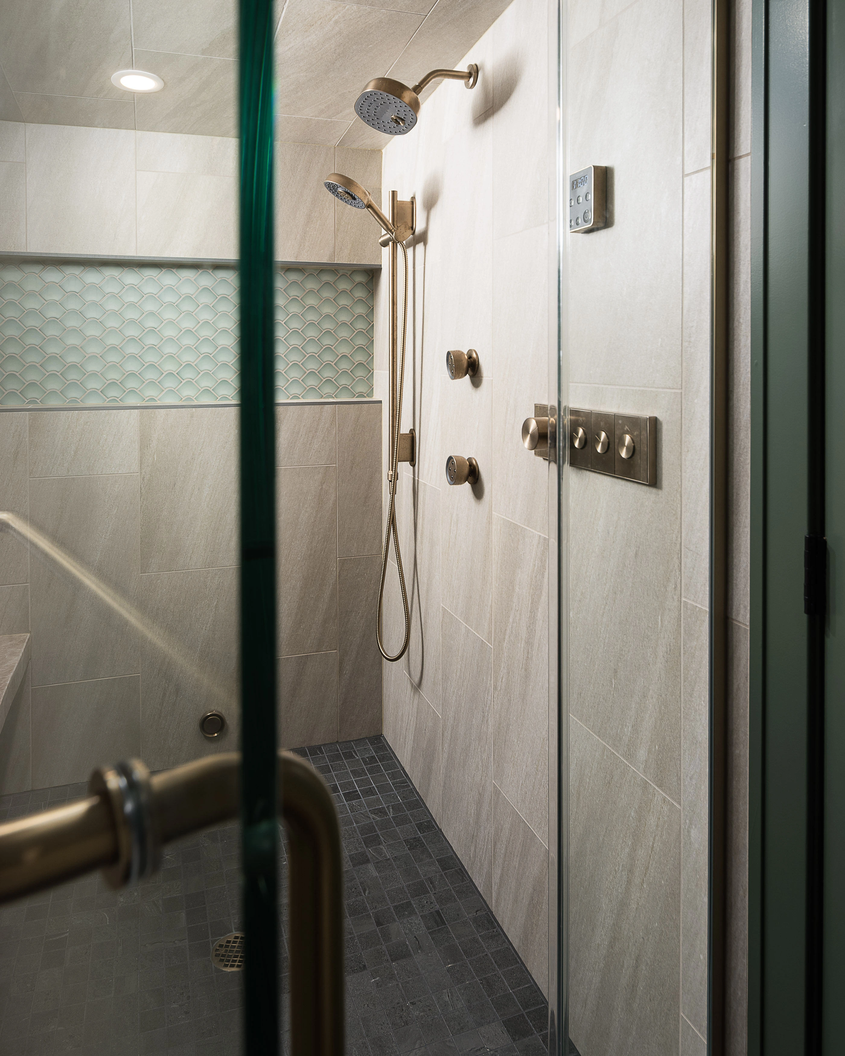 Modern shower with glass door, chrome fixtures, and beige tiles. Wall niche features decorative tile pattern. Cozy, contemporary bathroom space, elegantly designed.
