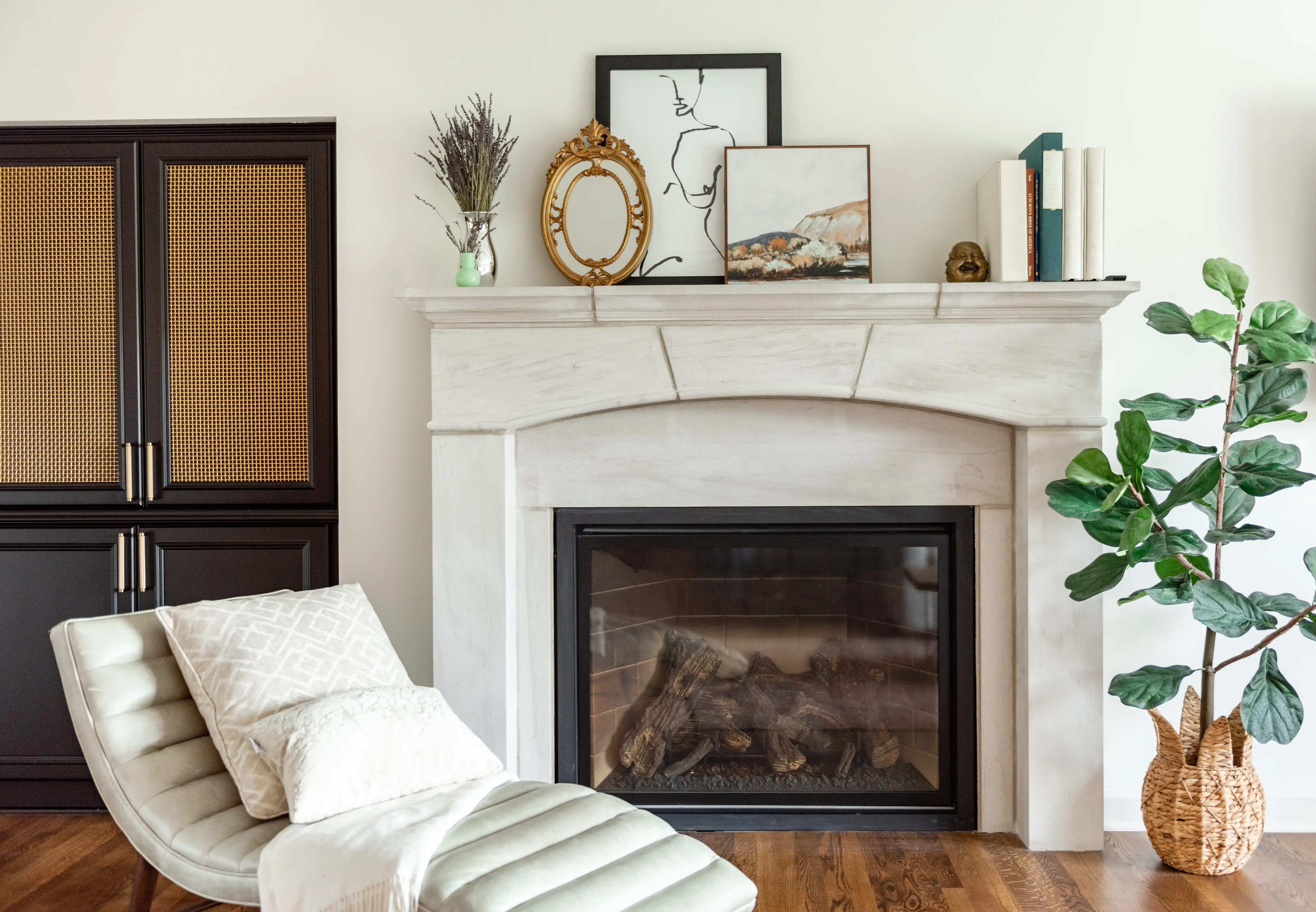 A tranquil living room features a white fireplace with artwork, plants, and books on the mantel, next to a modern lounger.
