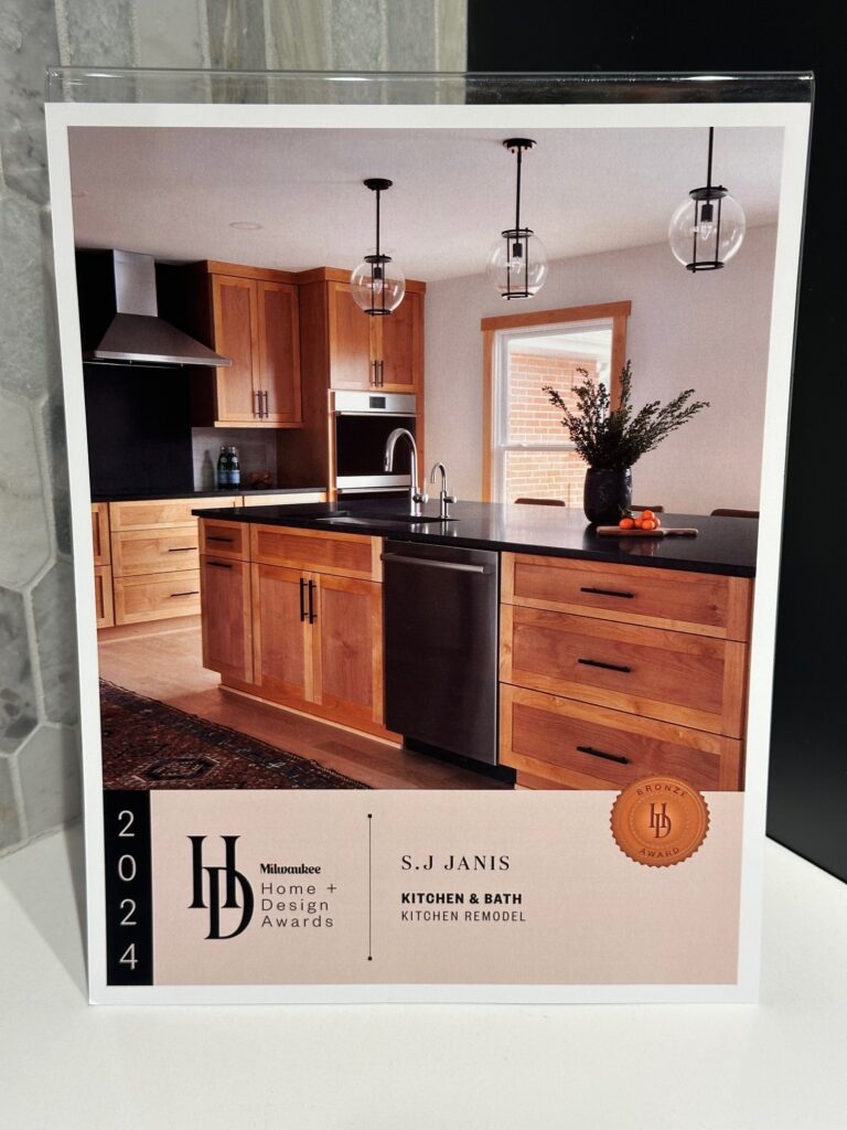 Modern kitchen remodel with wooden cabinets, sleek black countertops, and pendant lighting featured in a 2024 Milwaukee Home + Design Awards magazine page.