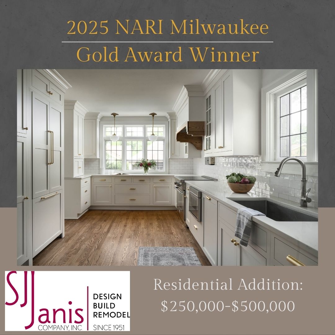 Spacious modern kitchen with white cabinets and wood flooring. Label highlights 2025 award-winning design by S.J. Janis Company, specializing in residential additions.