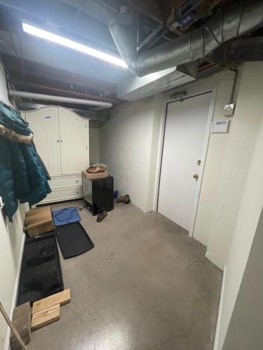 A basement hallway with concrete floors, white walls, a coat rack, and a wardrobe. Exposed pipes hang from the ceiling.