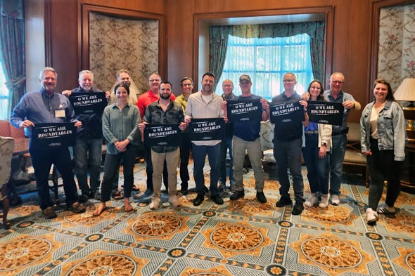 A group of people in a decorated room holding signs reading "We are hospitality allies," with patterned carpet and wooden panels.