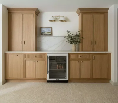 Wooden cabinets with a small beverage fridge, vase, and painting. Elegant lighting above. Soft carpet floor and closed doors on each side.