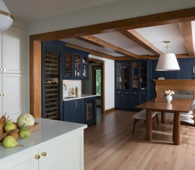 Elegant kitchen with dark blue cabinetry, wooden dining table, and white countertop. Fruit arrangement on island adds a touch of color.