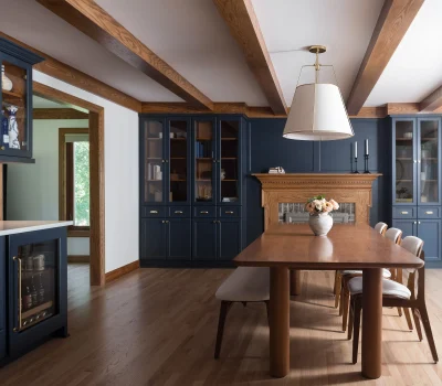 A dining room features elegant wooden beams, dark blue cabinetry, a large wooden table, and a modern pendant light.