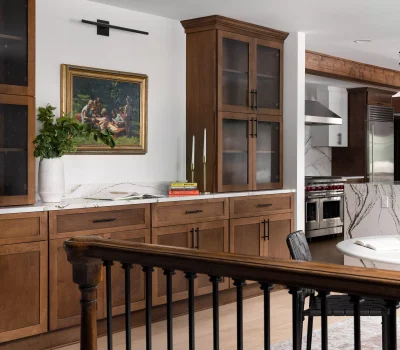 Modern kitchen with wooden cabinets, marble countertops, chandelier, and a painting on the wall. Round dining table with chairs in foreground.