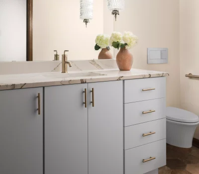 Elegant bathroom with a marble countertop, brass fixtures, and two vases with flowers. Hexagon floor tiles and decorative glass light fixtures.