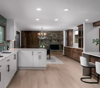 Modern kitchen with white cabinets, marble countertops, green tile backsplash, and wooden accents. Spacious layout with a stone fireplace and chandelier.