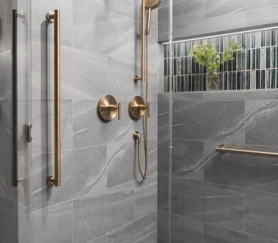 Modern shower with gray tiles, gold fixtures, and green plant in a glass-tiled niche. Clean, sleek design for a contemporary bathroom.