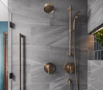 Modern bathroom shower with gray tiles, brass fixtures, glass door, and a niche with decorative plants in a glass jar.