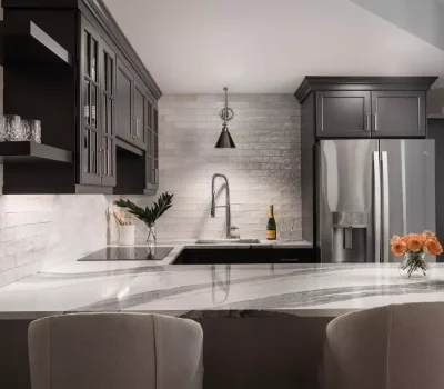Modern kitchen with dark cabinets, sleek countertops, and stainless steel appliances. Vase of roses and a champagne bottle add elegant touches.