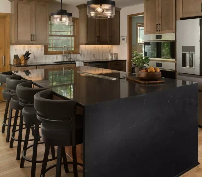 Modern kitchen features a large black island with bar stools, wooden cabinets, stainless steel appliances, pendant lights, and a window view.
