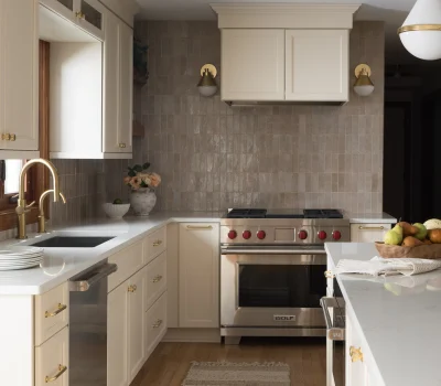 Elegant kitchen with beige cabinetry, marble countertops, stainless steel appliances, and gold accents. A striped rug and fruit bowl add warmth.