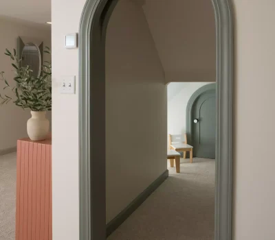 Minimalist interior with a green arched doorway, light decor, carpet, wooden chair, and potted plant on a red table. Calm ambiance.
